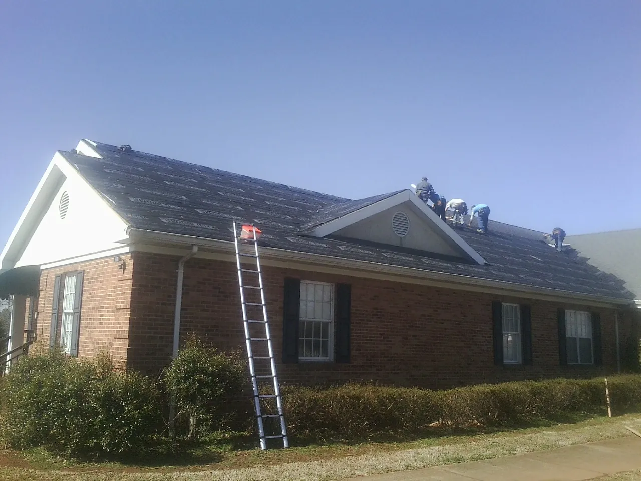 Crew tearing shingles off a brick ranch roof with a ladder set — Metal Roof Repair work by our crew in Minerva
