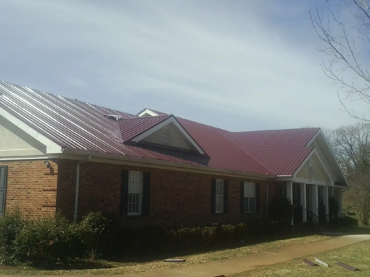 Red metal roof with gabled entries on a long brick building, from a Hail Damage Roof Repair job in Minerva