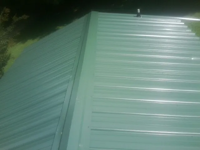 New green metal panels meeting at the ridge of a roof — Flat Roof Repair work by our crew in Minerva