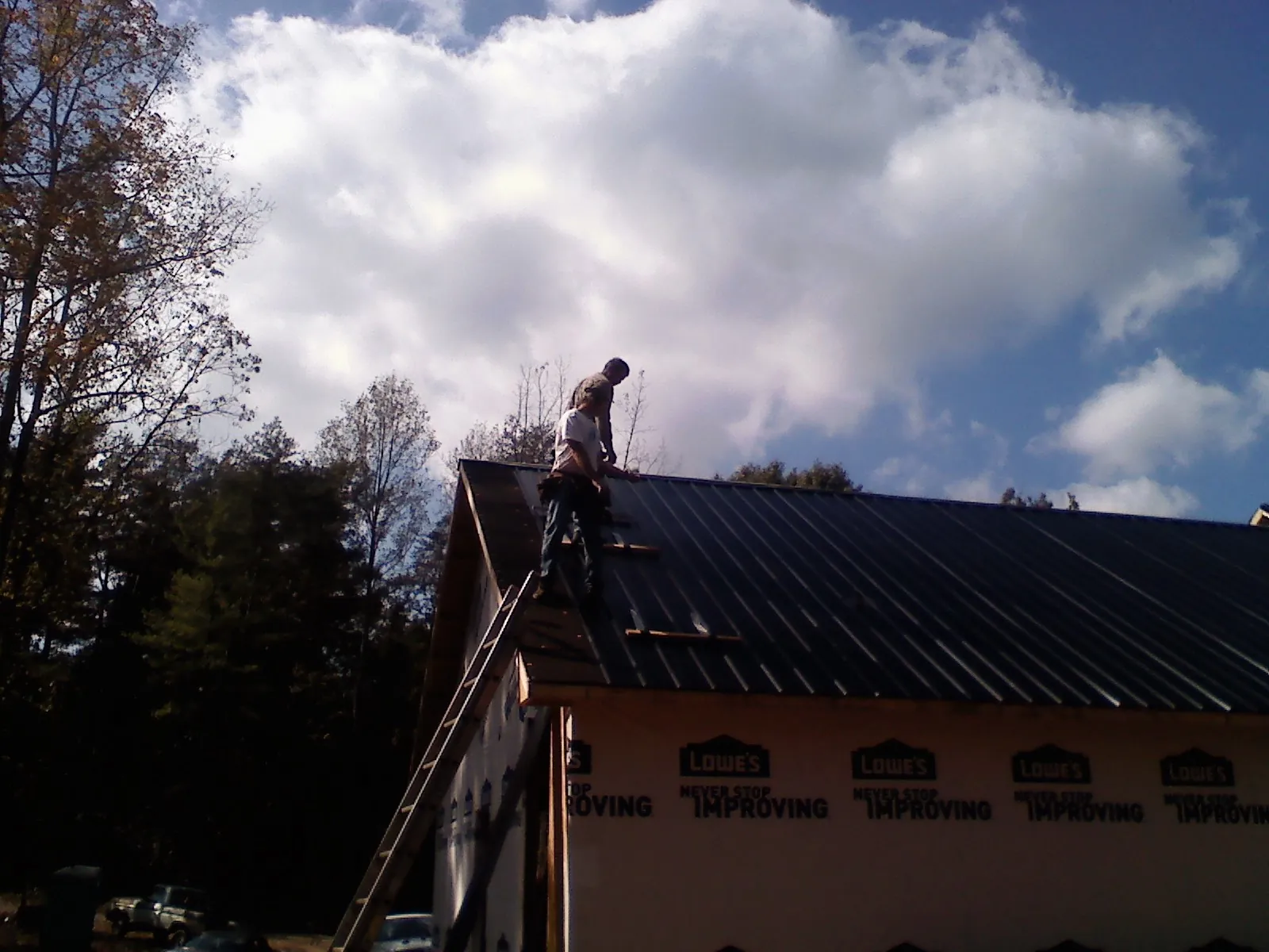 Roofer fastening dark metal panels high against a cloudy sky, from a Roof Inspection job in Minerva