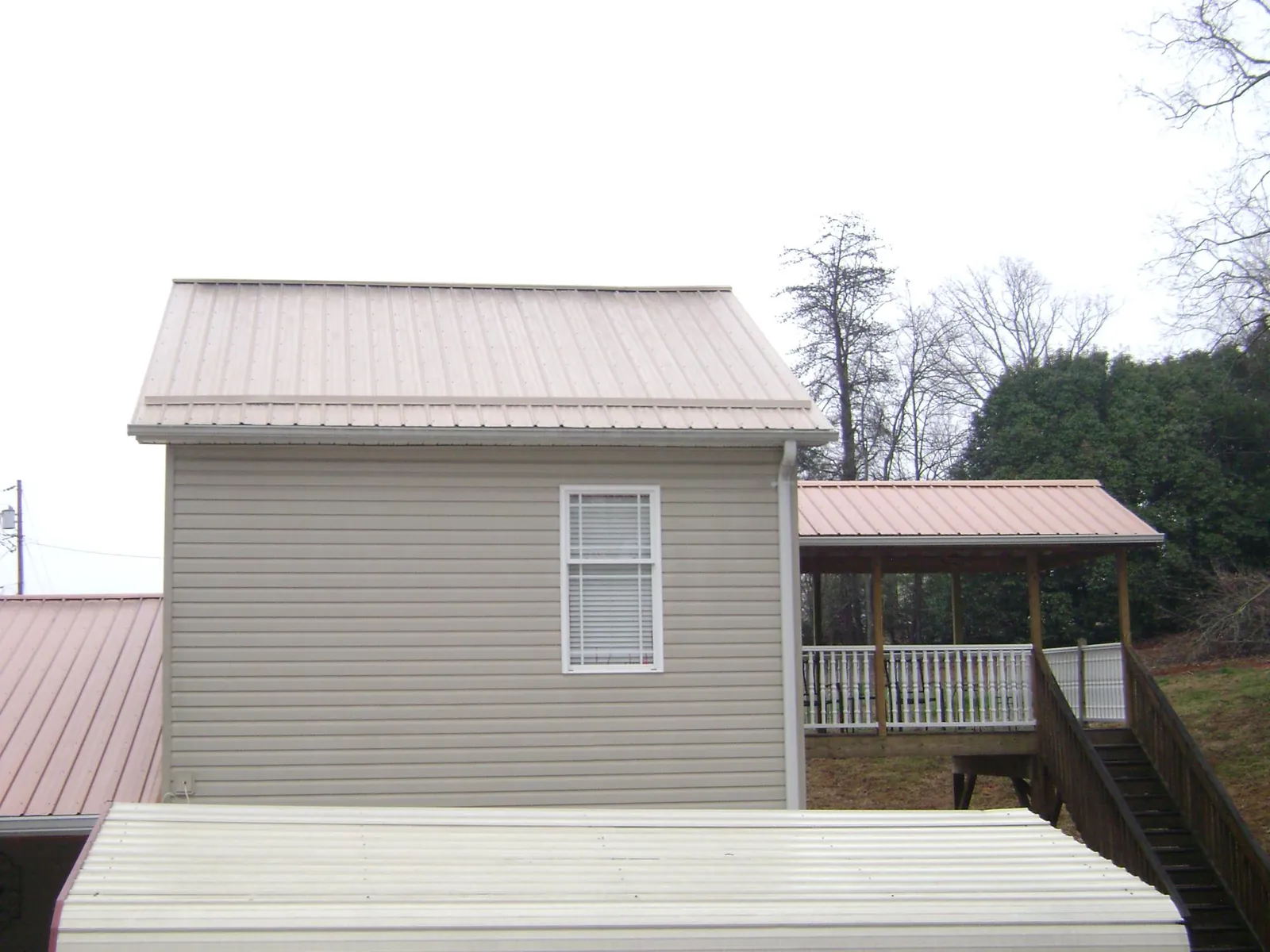 Tan metal roofs on a two story addition and attached porch, from a Roof Replacement job in Minerva